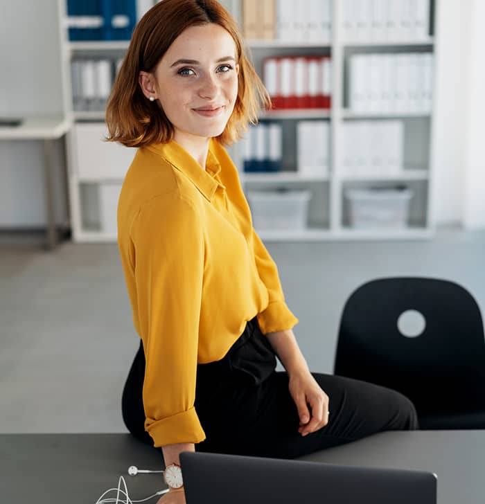 Eine lächelnde Frau sitzt vor dem Laptop im Büro